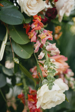 Detail shot of cascading white roses and pink snapdragons among greenery on a ceremony arch. This stunning floral arrangement reflects the charm and elegance of a southern backyard wedding in Savannah