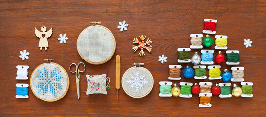 Winter craft and Christmas handmade gifts concept. Flat lay of funny unusual Christmas tree made from colorful threads on bobbins, and hand embroidered cross stitch snowflakes in hoops on wooden table
