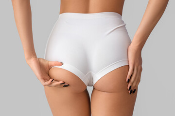 Young woman in underwear with cellulite problem on light background, back view