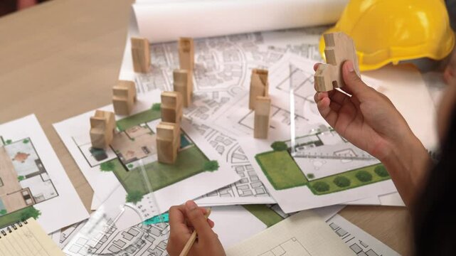 Architect and engineer consider or discuss about building construction using blueprint on table with architectural document, measurement tool and wooden block scatter around at office. Delineation.