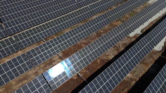 Low aerial orbit over bifacial solar panels producing energy at Solar Farm in Finland, dirt and gravel shown between rows