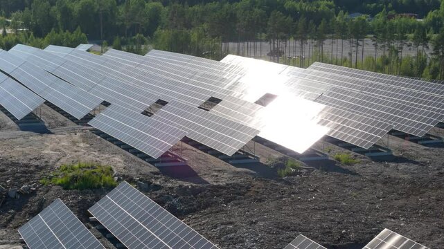 Aerial orbit across Solar Farm in Finland, showcasing rows of bifacial panels producing energy as sunlight glistens above dry ground on glass