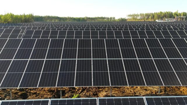 Aerial low dolly over of Solar Farm highlighting rows of bifacial solar panels sweeping out to horizon