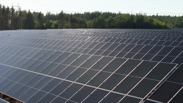 Aerial trucking pan right over Solar Farm bifacial panels producing renewable energy in Finland, evergreen trees in backdrop