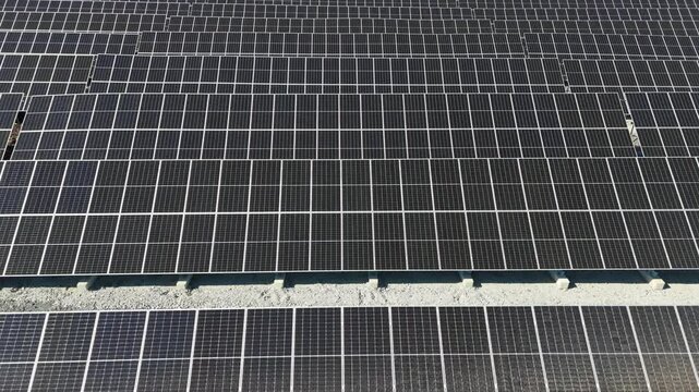 Aerial pan over Solar Farm showcasing bifacial panels producing renewable energy in Finland, textured perfect rows in stunning column out to tree line, industrial grid pattern