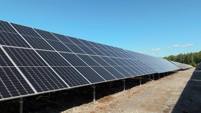Low detailed angled dolly of bifacial solar panels reflecting sunlight at Solar Farm in Finland, eye level walking POV