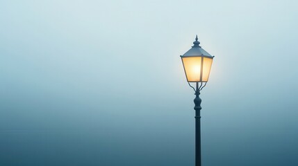 Fototapeta premium A solitary lamp post shines softly in a foggy atmosphere, creating a serene and mysterious ambiance.