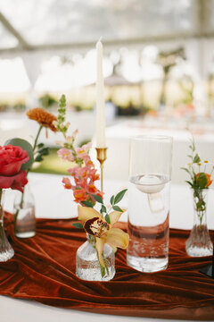 Autumn wedding tablescape with terracotta velvet and vibrant florals including with red roses and snapdragons, and gold candlesticks