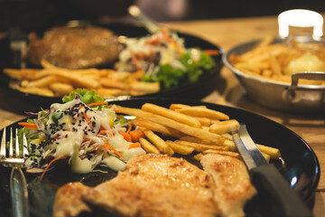 Vegetable salad and french fries and steak in a black plate on a wooden table. close up