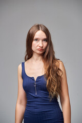 Fototapeta premium A woman in a blue dress stands on a gray background. She has long hair and a slender body.