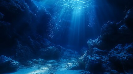 A shaft of sunlight illuminates the dark blue depths of the ocean, revealing a rocky underwater landscape.