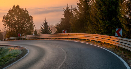 Winding asphalt road with barriers during spectacular sunrise above low lying mists