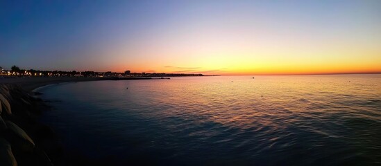 Obraz premium Serene sunset view illuminating a tranquil beach with calm waters and vibrant sky colors