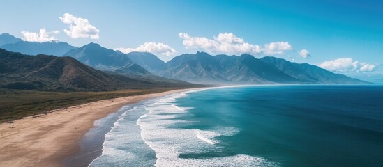 Naklejka premium Drone view of a pristine beach showcasing turquoise waters and majestic mountains under a clear blue sky on a beautiful summer day