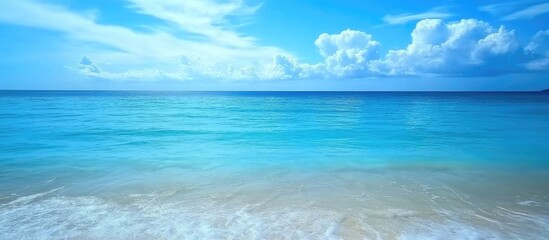 Obraz premium Tranquil blue ocean waves gently lapping at a sandy shore under a bright sky with soft clouds and serene turquoise water.