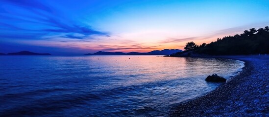 Fototapeta premium Serene twilight over calm blue sea with gentle waves and vibrant sky at dusk reflecting nature's beauty and tranquility.