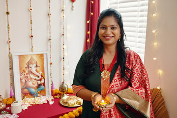 Portrait of woman celebrating Diwali with traditional decor, holding an oil lamp. Ganesh idol, festive garlands, and colorful offerings adorn surroundings