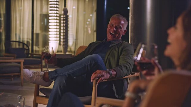 Mature couple laughs with friends around a fire pit while drinking wine