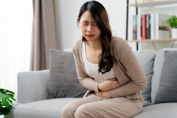 A woman is sitting on a couch holding her stomach with a stomach ache. Healthcare and medical.