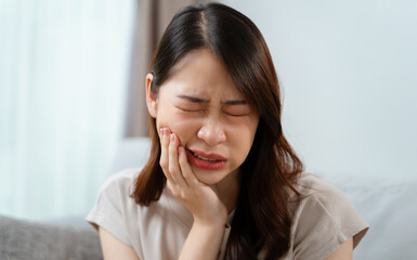 A woman is in pain and is holding her face having a toothache. Healthcare and medical concept.