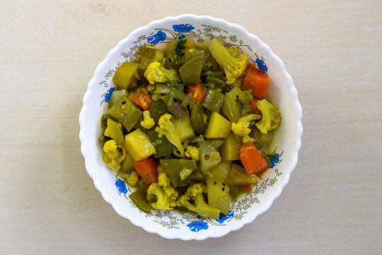 Healthy vegetables curry in a white bowl on a wooden surface, featuring a variety of mixed vegetables including cauliflower, carrots, beans, snake gourd, potatoes, pointed gourd, cucumbers. Top view.