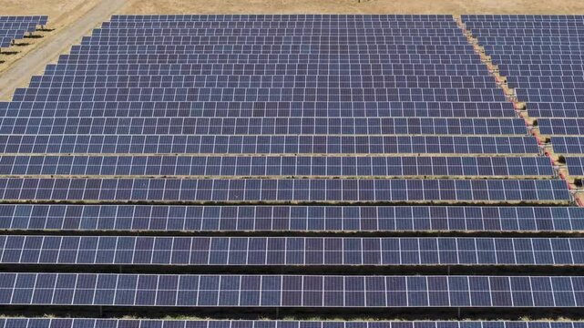 Aerial pull of symmetrical solar panel rows in a barren grass field