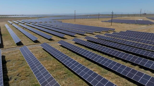 Aerial pull pan of solar panel rows in a barren grass field