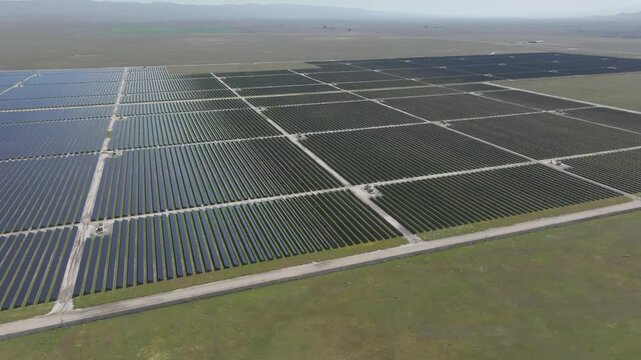 Panning aerial drone footage of large solar farm amidst green fields