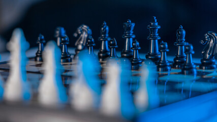 Chess game and board. Two rows of black and white figures of chess game at the beginning. Blue and white modern lighting.