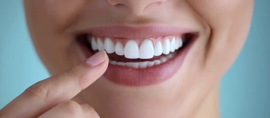 Obraz premium Beautiful woman pointing her finger at her perfect white teeth, with a close-up of her mouth and fingers against a light blue background, featuring a banner ad.
