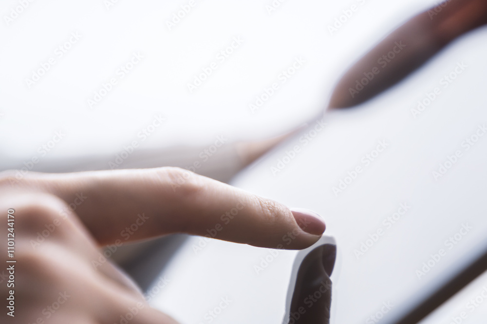 Poster closeup view of a female finger operating a high-tech tablet on a desk, set against the blurred back