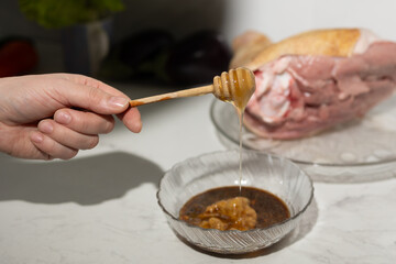 A person is carefully pouring honey into a bowl filled with food - pork knuckle, enhancing the dishs sweetness and flavor with this delicious ingredient