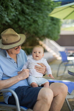 Grandfather and infant grandson on his lap on a pool deck