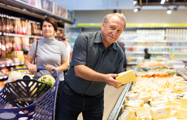 Elderly man choose cheese in supermarket
