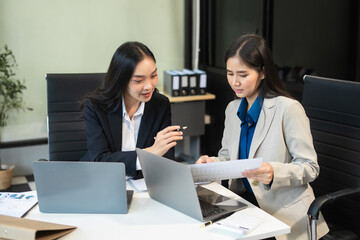 Asian manager mentor talking to young Asian female coworker, showing online project results at meeting. Two happy diverse professional executives team working in office using pc laptop.