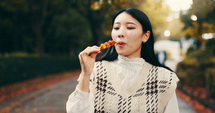 City, japanese woman and eating street food in park for traditional dessert, lunch and cultural cuisine. Tourist, hungry person and enjoyment with dango dumpling, skewer snack and sweets taste test