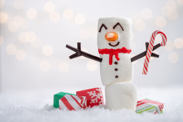 A snowman with a candy cane is standing in front of a pile of presents