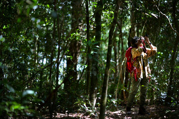 Middle age woman in her camouflage suit and big red backpack explore the forest with her camera in hand. She slowly walking around and taking some photo.