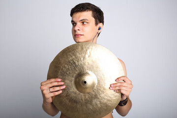 A young male drummer holding a golden ride cymbal, partially shielding. Concept of modern music with drum set, a drummer career in a band, musical hobbies and drumming techniques and education