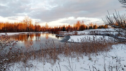 Winter scene with reflections in water and sunset color on tree. Frosted trees against a blue cloudy sky during winter