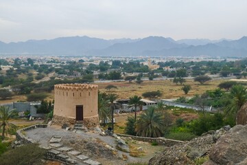 Obraz premium Watch Tower on blurred cloudy mountains background next to historical oldest AL Bidyah Mosque, Fujairah. UAE .Popular touristic weekend travel destination.
