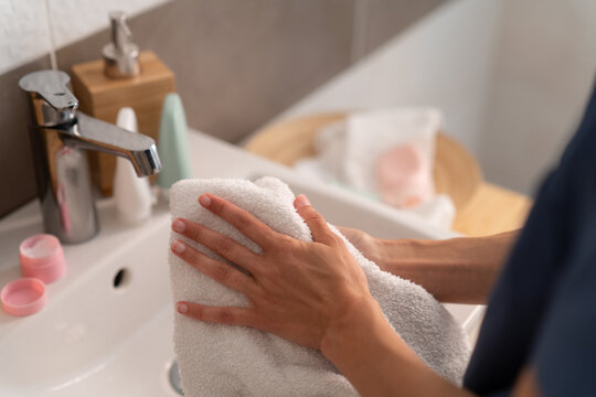 Close-up of a woman standing at a bathroom sink drying  her hands with a towel