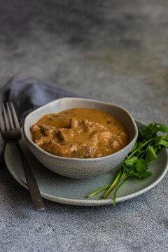 Close-up of a bowl of beef stroganoff with fresh coriander and a glass of white wine