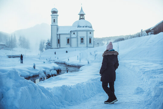 Woman standing the winter snow looking at Seekirchl (Heiligkreuzkirchein), Seefeld, Tyrol, Austria