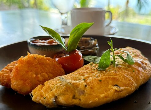 Omelette, hash browns, baked beans and tomato breakfast with a cup of tea and glass of water