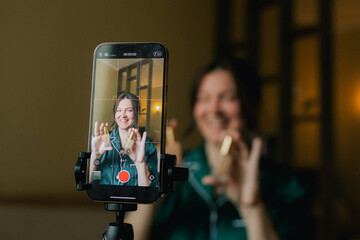 Plus size woman applying makeup on face with brush while recording vlog on smartphone for social...