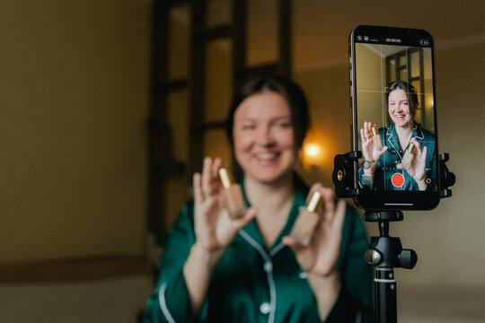 Plus size woman applying makeup on face with brush while recording vlog on smartphone for social media. Multiethnic fashion makeup artist vlogger live streaming makeup tutorial. Part of a series. UGC