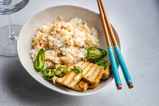 Overhead view of a bowl of Rice with slices of barbecued tofu cheese, fresh chillis and soy sauce