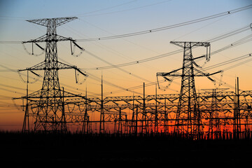 Fototapeta premium Many high-voltage power towers, silhouetted against the setting sun