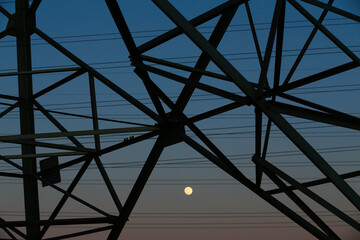 Many high-voltage power towers, silhouetted against the setting sun